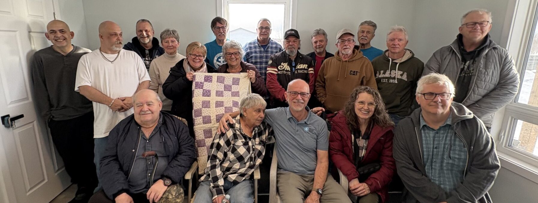 Group of about 15 people pose together for a picture inside a newly constructed house.