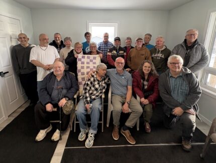 Group of about 15 people pose together for a picture inside a newly constructed house.