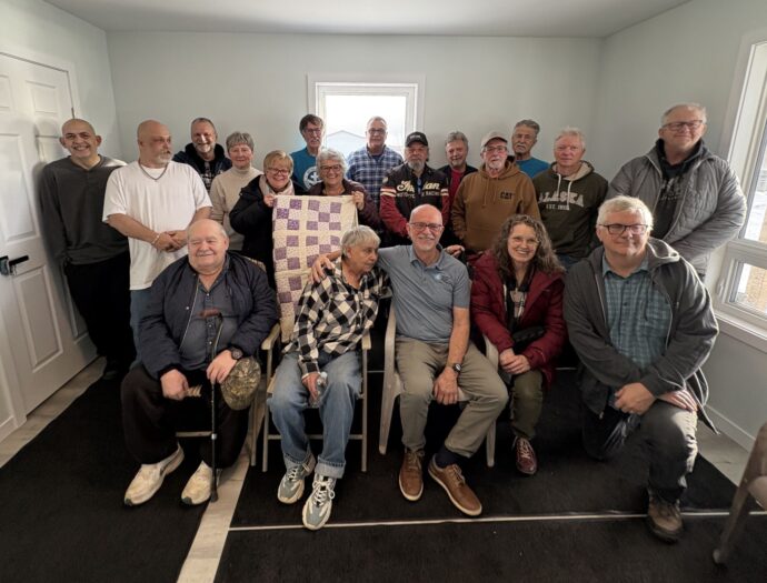 Group of about 15 people pose together for a picture inside a newly constructed house.