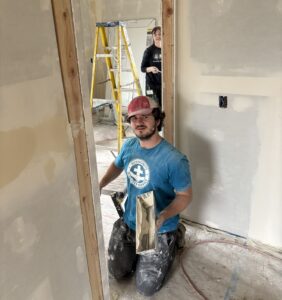 Man kneels in doorway while working on patching home