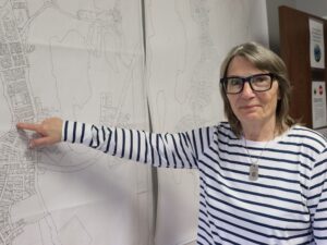 Woman stands beside a map, pointing to a spot on it.