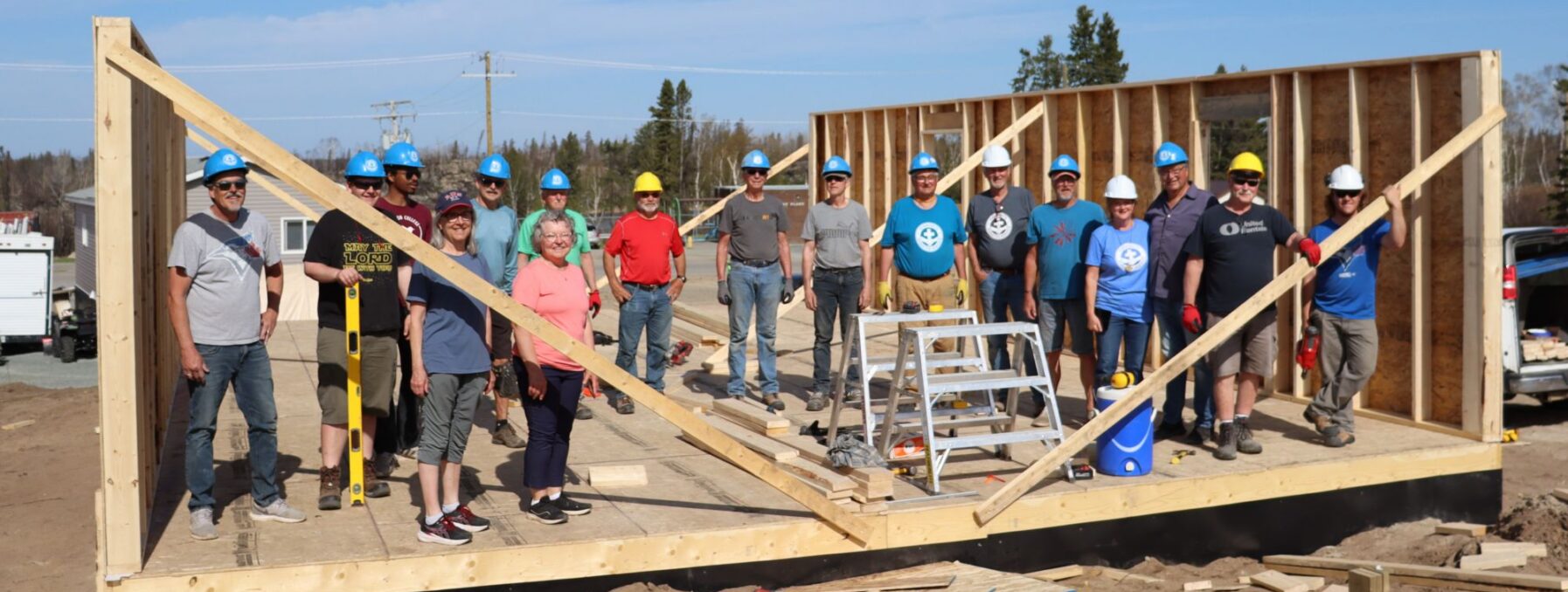 Group of people stand, posing for picture, inside a half-framed house.