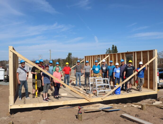 Group of people stand, posing for picture, inside a half-framed house.