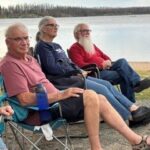 MDS volunteers sit in lawn chairs next to a lake.